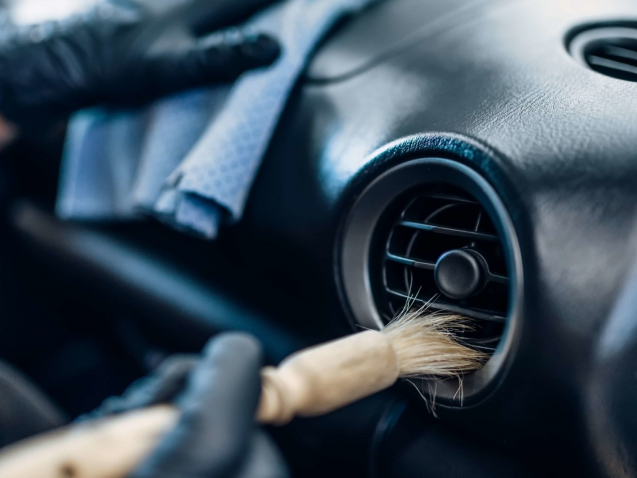 Auto detailing of car interior on carwash service. Worker in gloves cleans salon with brush