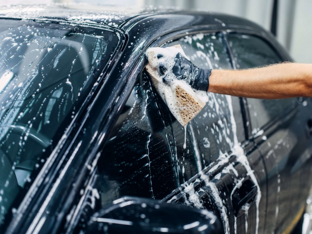 Carwash service, car cleaning, front view. Auto detailing, worker soaps glasses